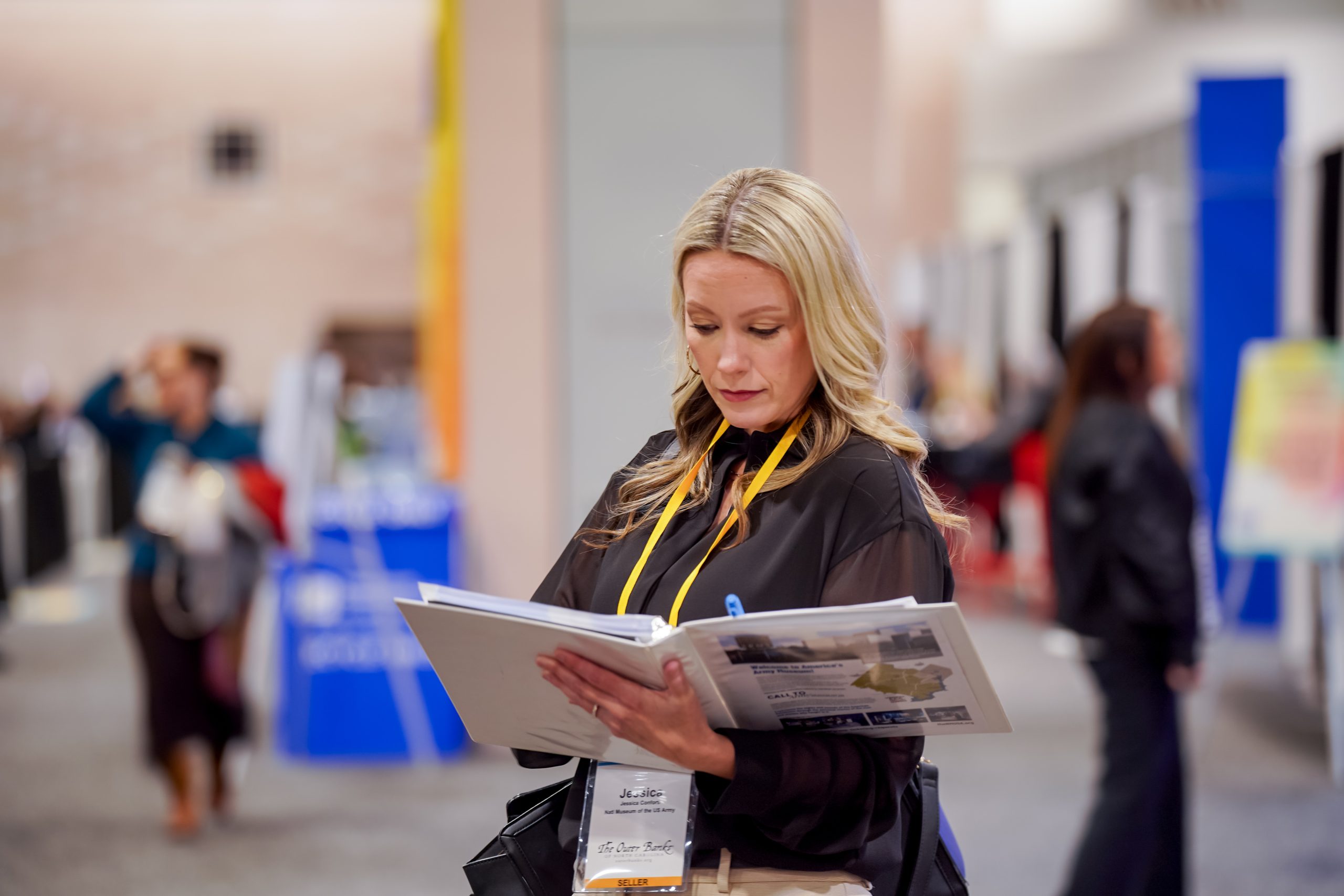 An image of a woman standing at a motorcoach industry event. She is holding a binder and reading its contents.