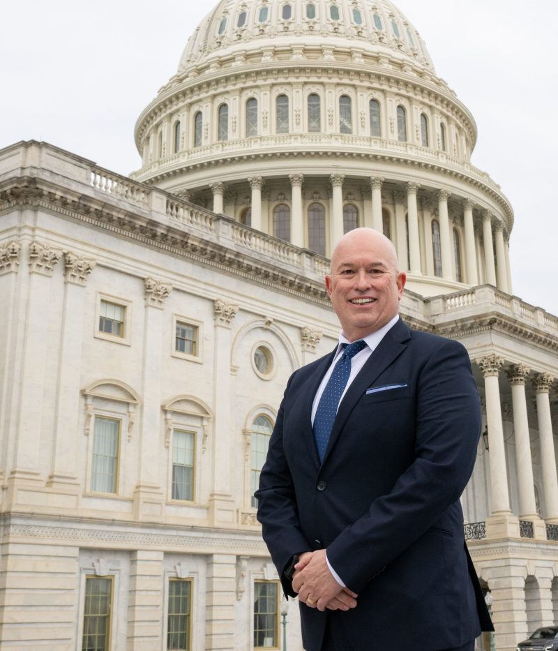 Latino man in blue suit and tie stands in front of the US Capitol building.